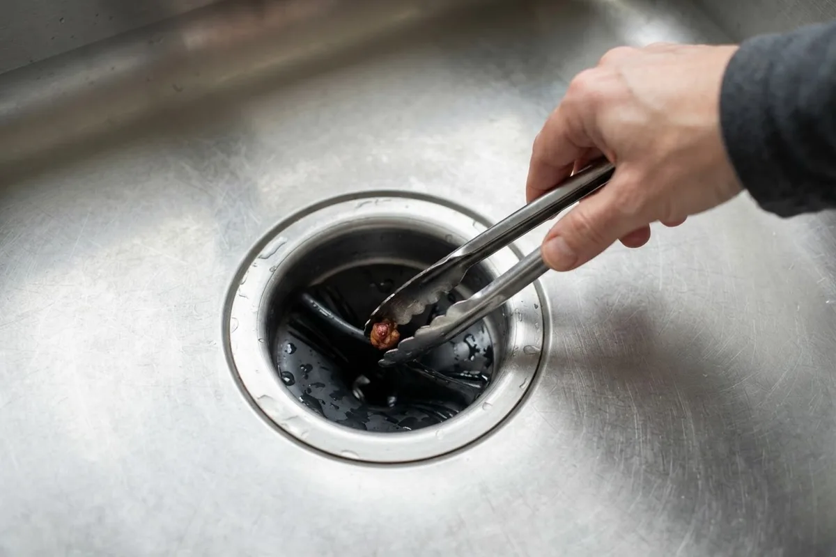 Using tongs to clear a jam when troubleshooting why is my garbage disposal smoking